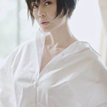 A woman dressed in a white shirt and jeans poses elegantly, embodying a relaxed and fashionable look.
